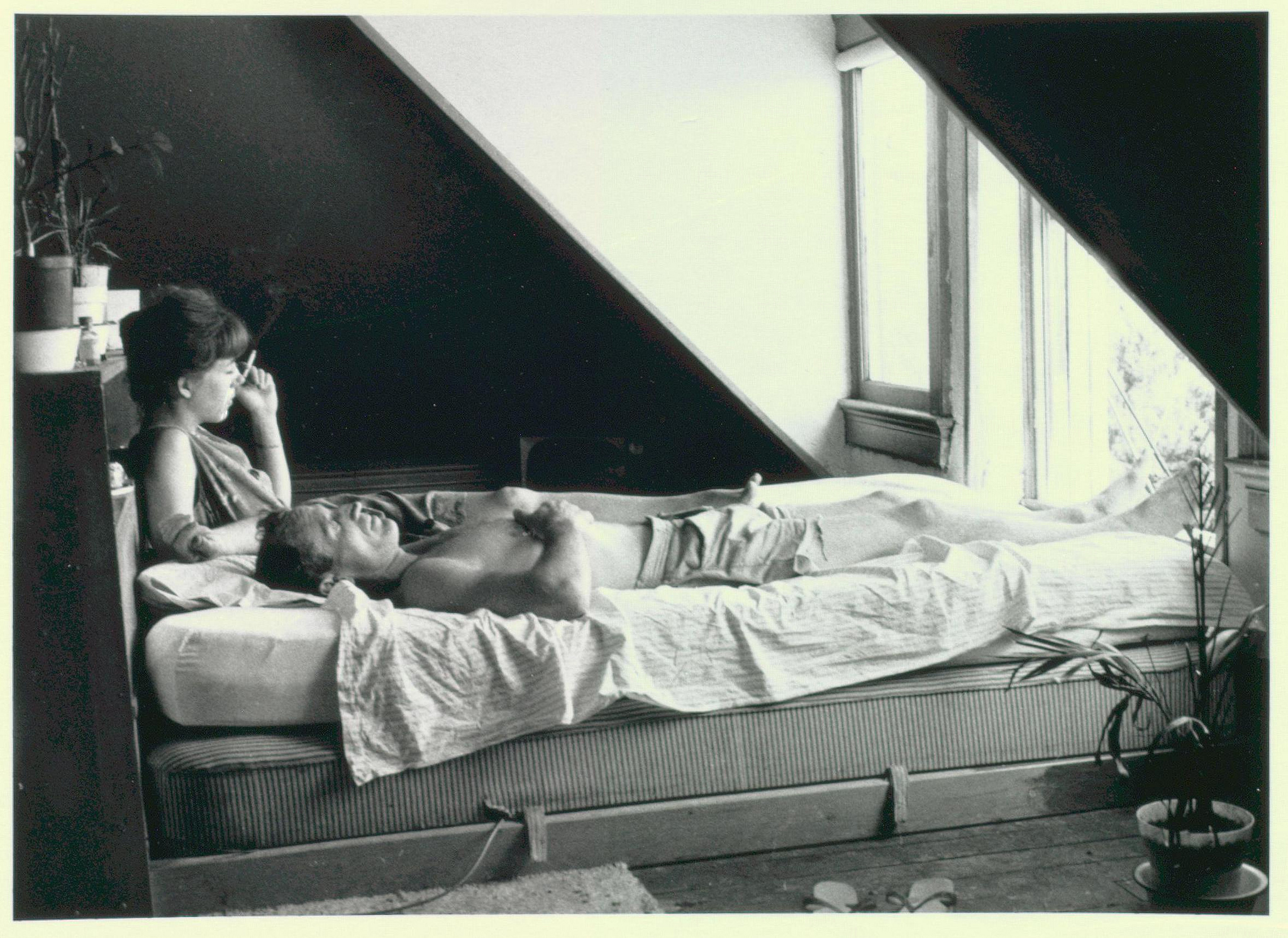 Neal Cassady in Millbrook, NY reclining on bed with lady friend, 1964