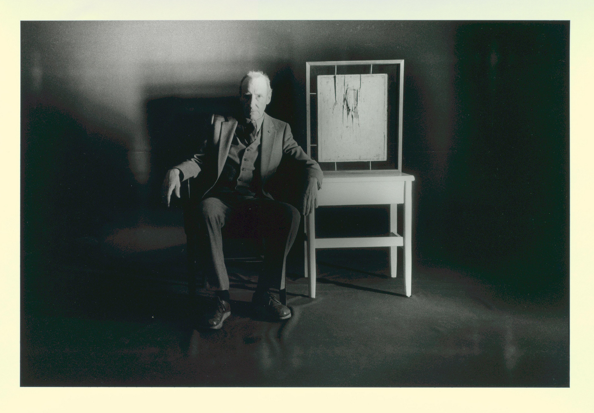 William Burroughs in studio seated next to chair, 1984